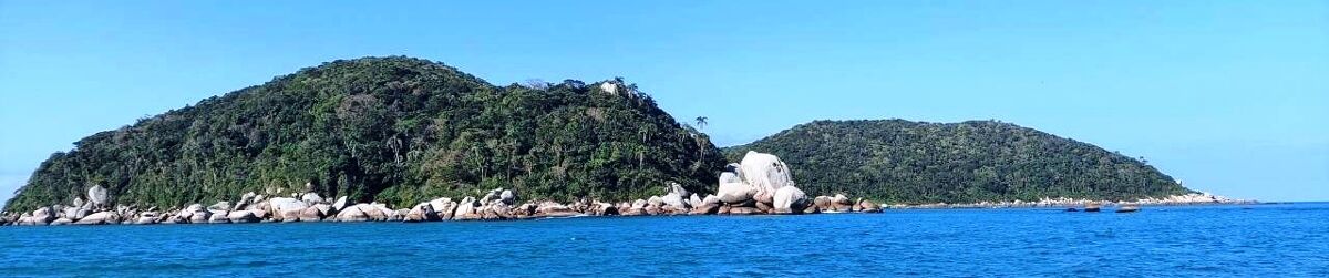 Costão da Ilha do Macuco visto do mar, com o barco de passeio ancorado.